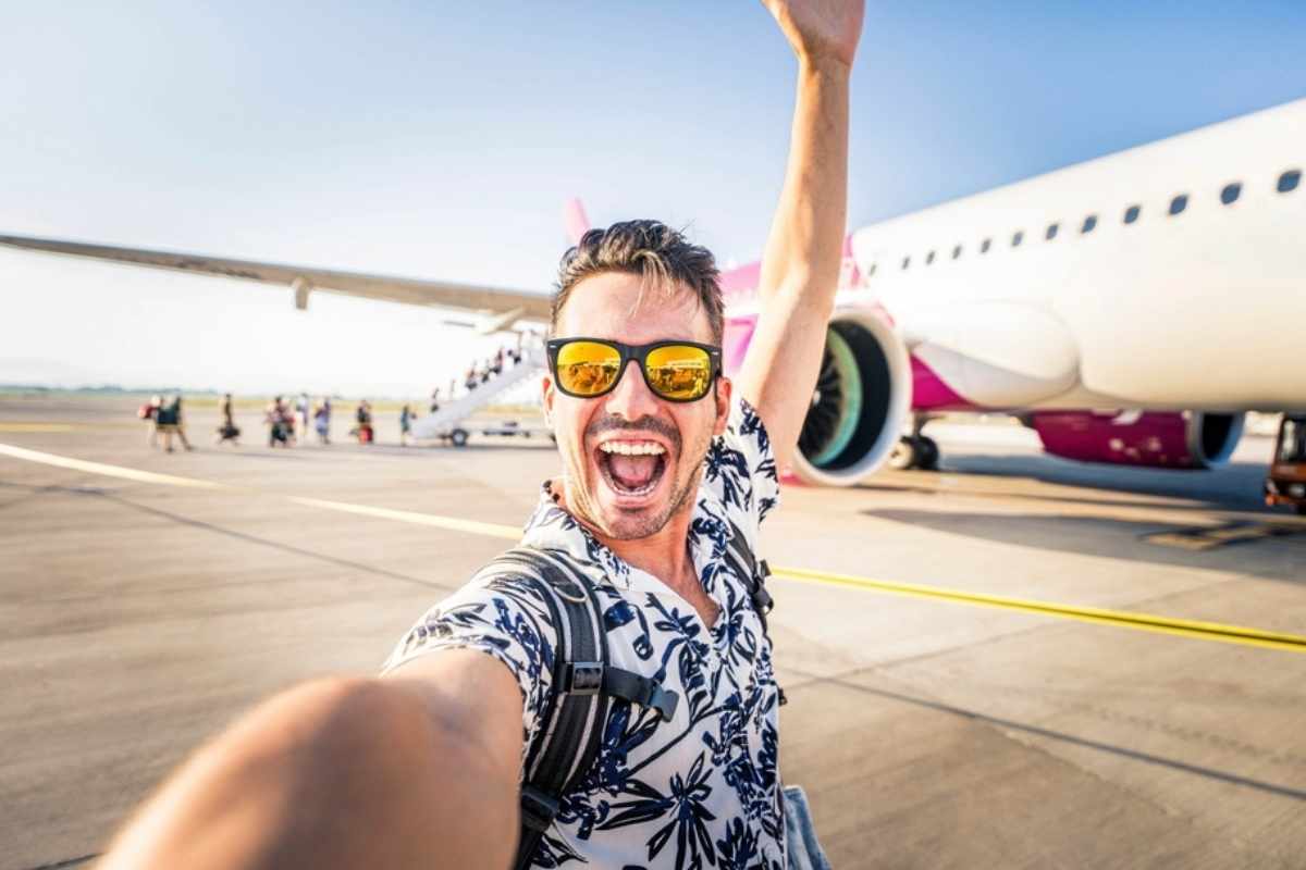 Seflie di uomo su pista di atterraggio con aereo su sfondo