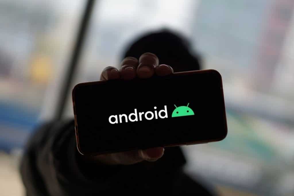 logo android su smartphone con sfondo nero in mano ad un ragazzo sullo sfondo