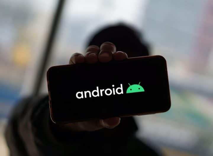 logo android su smartphone con sfondo nero in mano ad un ragazzo sullo sfondo